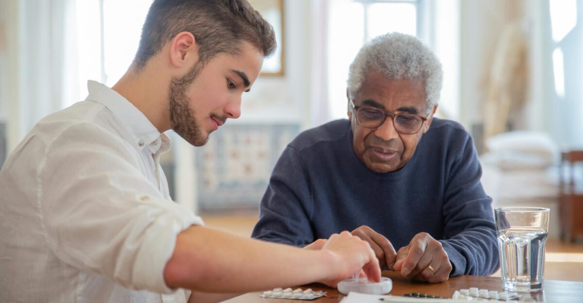 A young volunteer helps an elderly man manage his medication at a nursing home