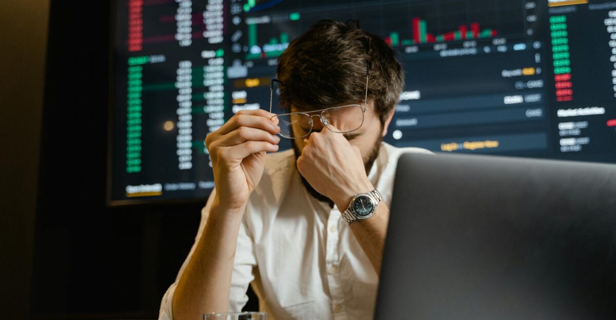 A stressed man looks at stock market data on his computer screen in an office setting