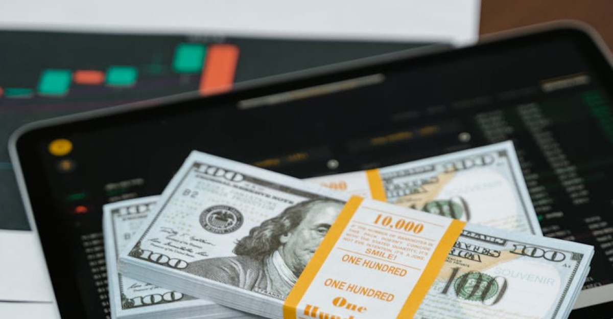 Stack of 100 bills placed on a tablet with financial graphs symbolizing digital finance