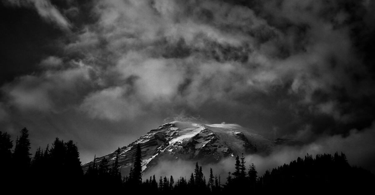 A stunning black and white photograph of Mount Rainier with dramatic clouds overhead.