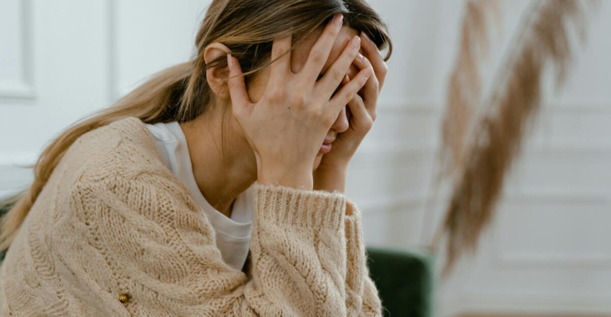 A woman sitting indoors covering her face in frustration depicting stress and mental health challenges
