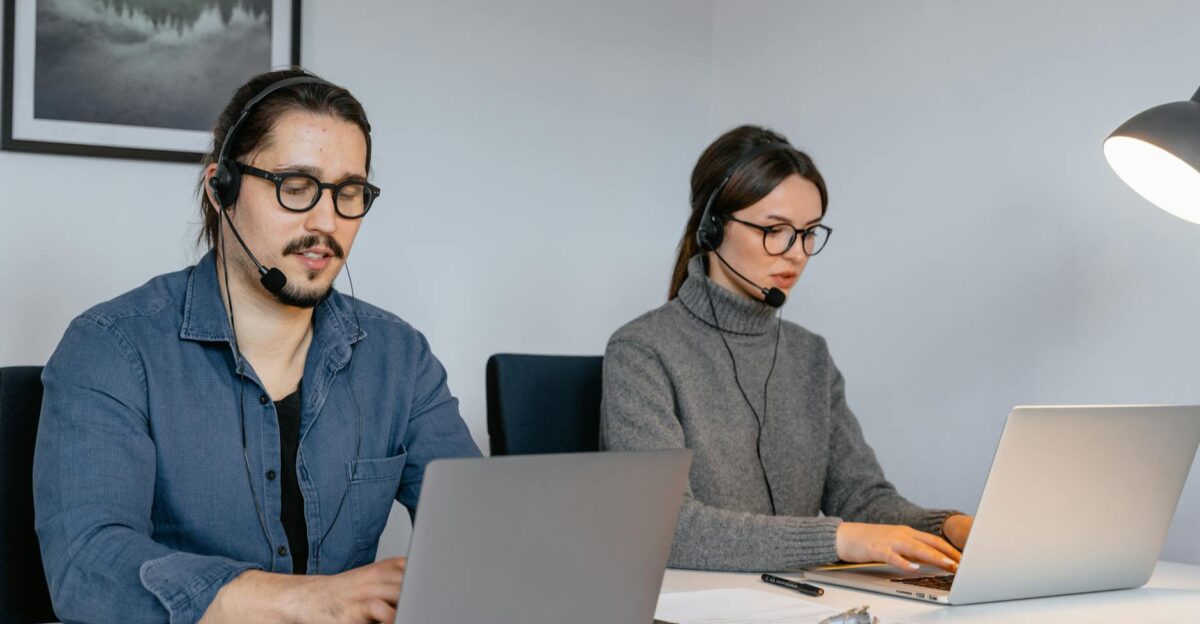 Two focused call center agents working on laptops with headsets in an office setting