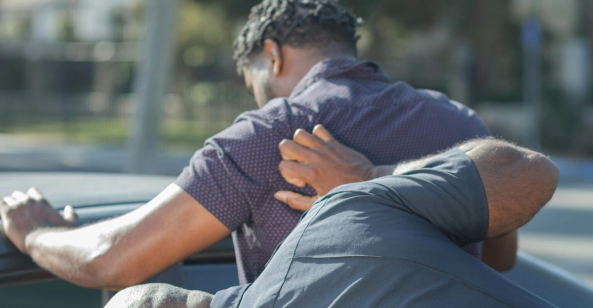 Police officers searching a suspect by a car for public safety and law enforcement.