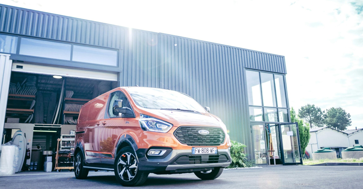 Low angle shot of an orange Ford Tourneo van parked outside a modern industrial building.