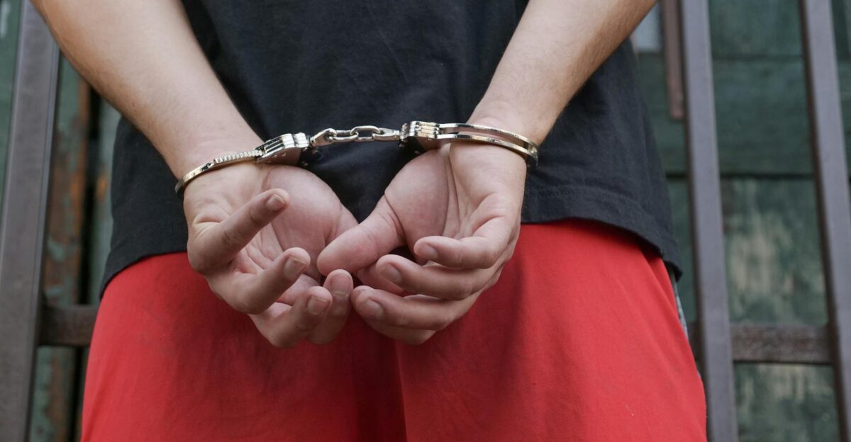 Close-up of a person in handcuffs viewed from behind wearing red pants and a black shirt