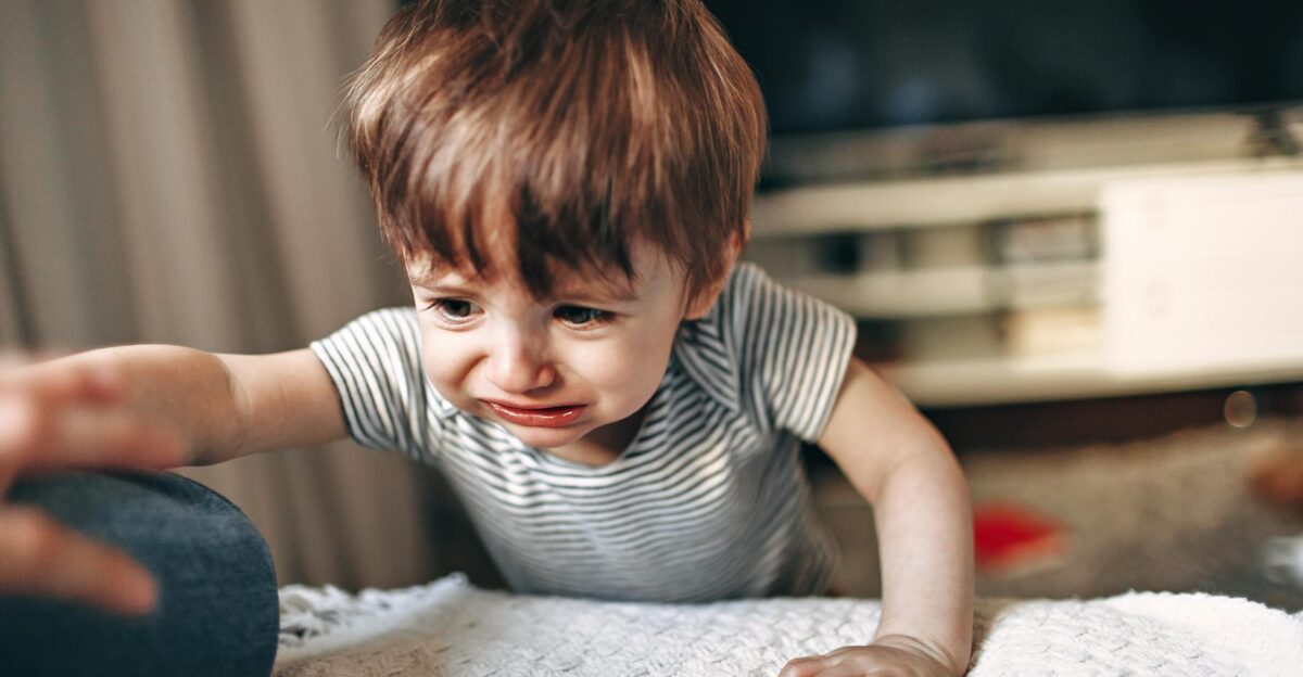 A young child in a striped shirt reaching out with a tearful expression indoors