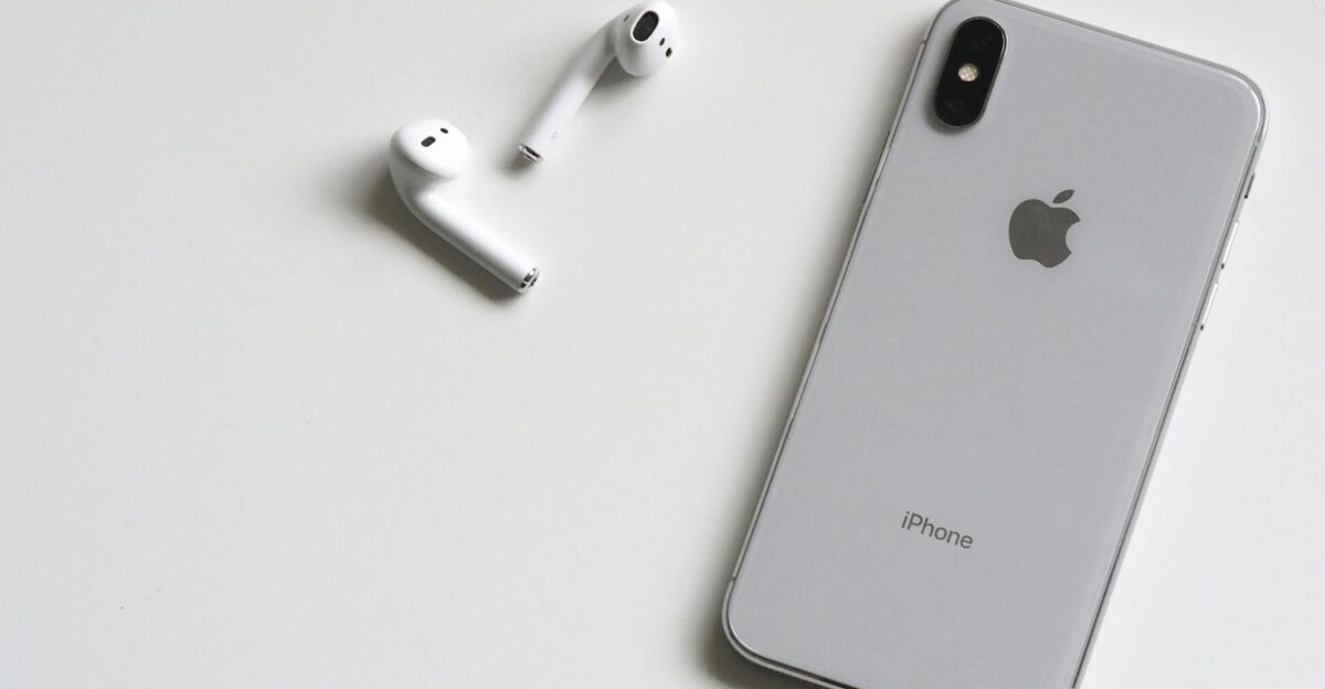 Close-up of a silver iPhone and wireless AirPods on a sleek white background