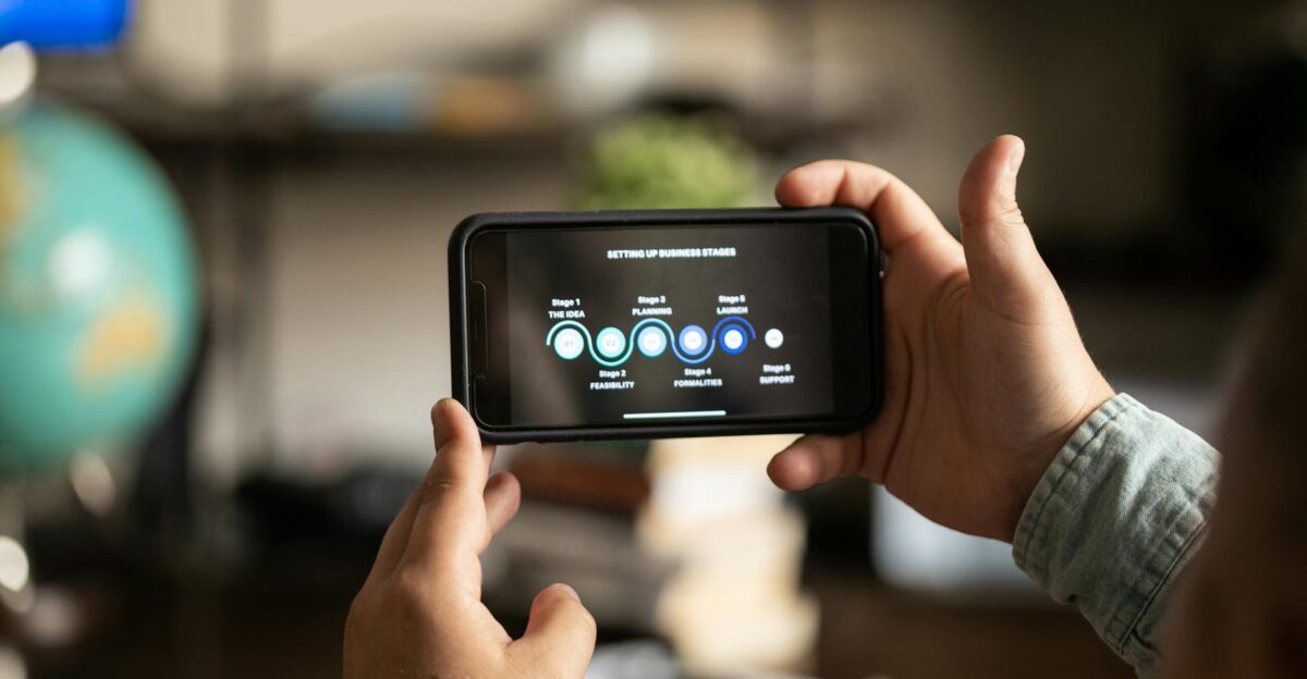 Hands holding a smartphone displaying business stages in a cozy indoor setting