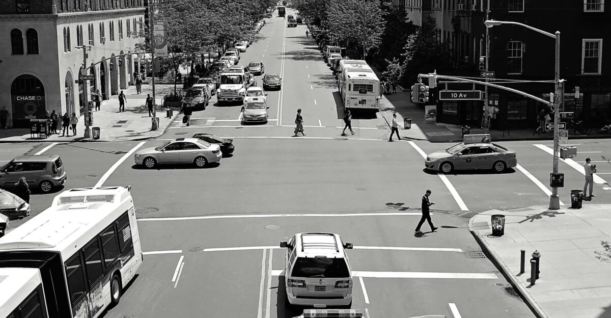 Black and white view of a busy street intersection in New York City with cars buses and pedestrians