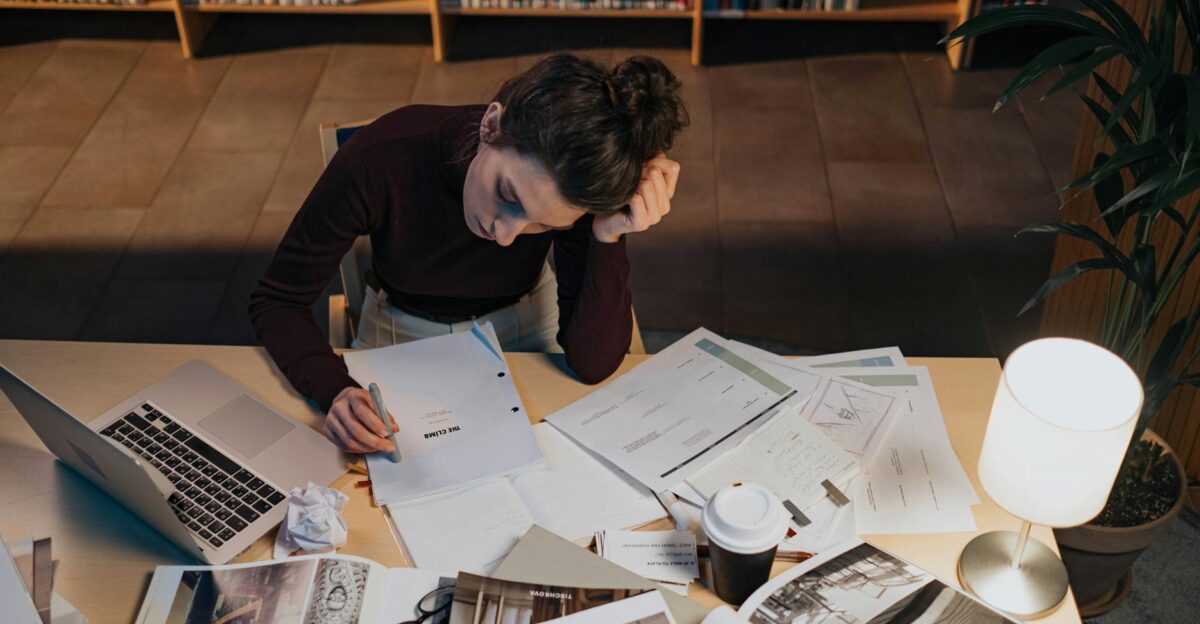 Woman studying at desk with documents laptop and coffee in a cozy library setting