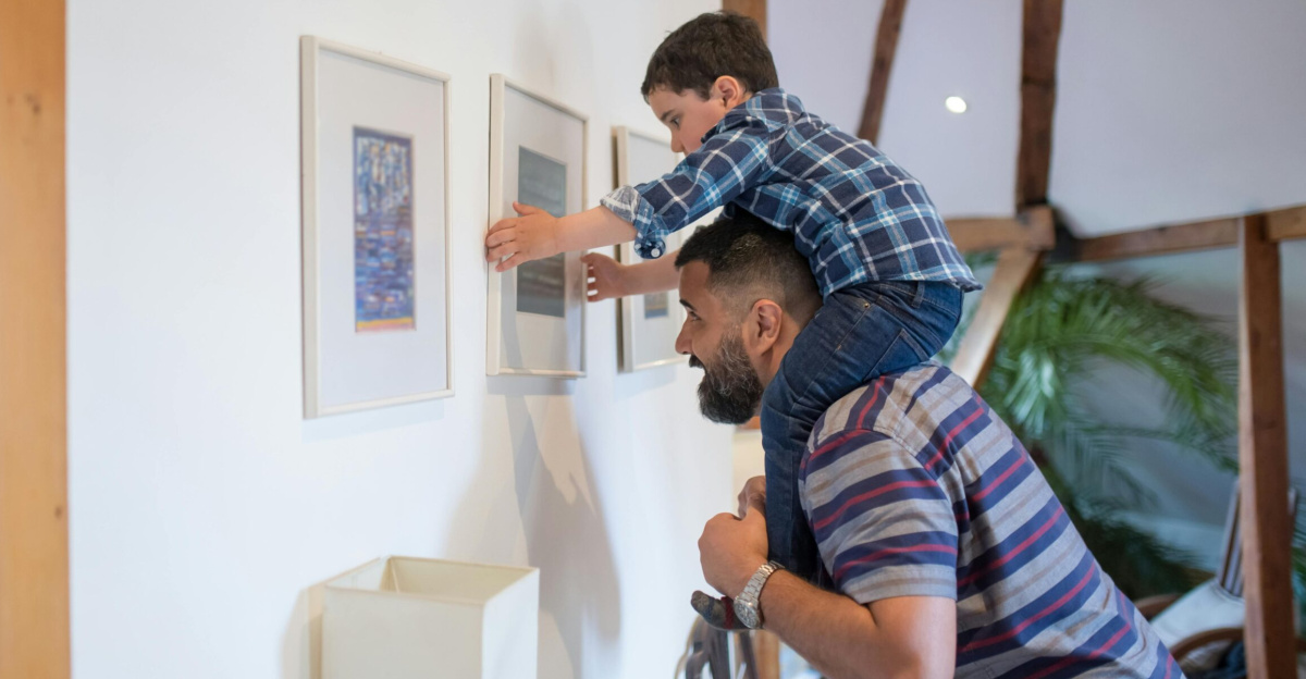 A father helps his son hang frames on the wall in their cozy home.