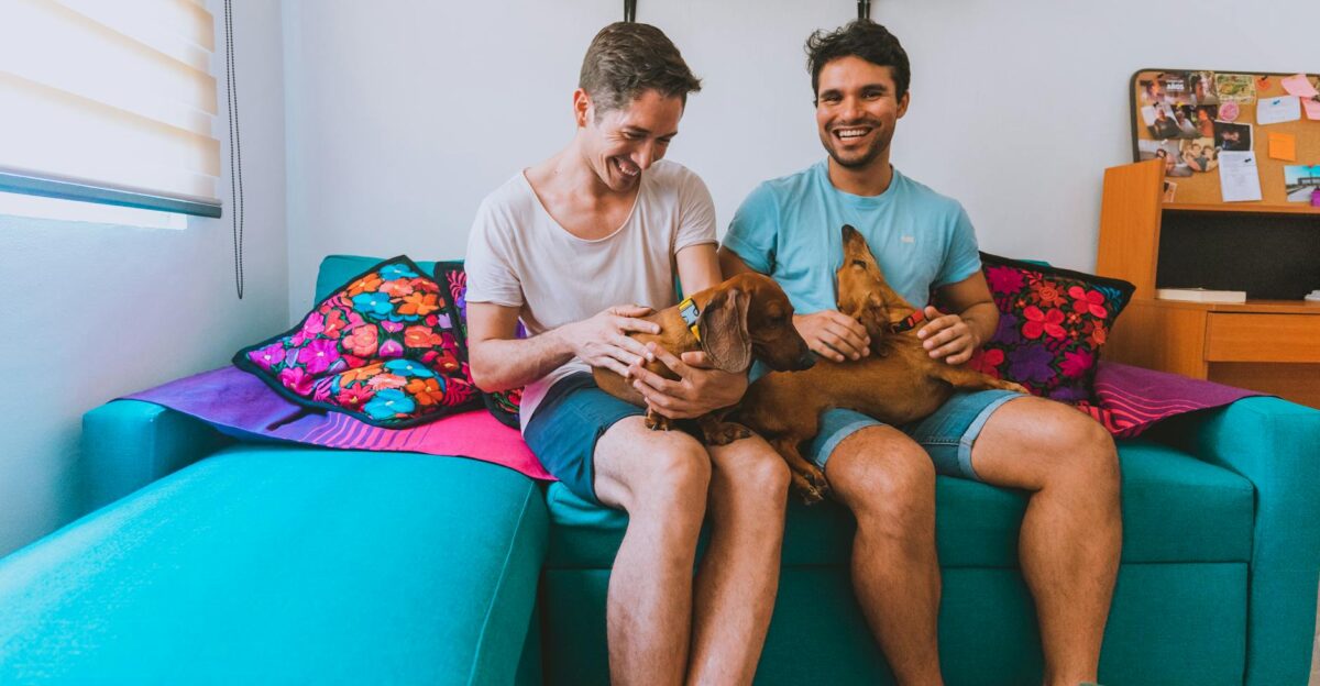 A joyful couple sitting at home on a couch playing with their dachshunds