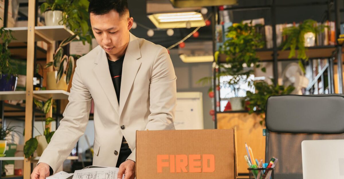 An employee packing documents into a box labeled FIRED in an office environment