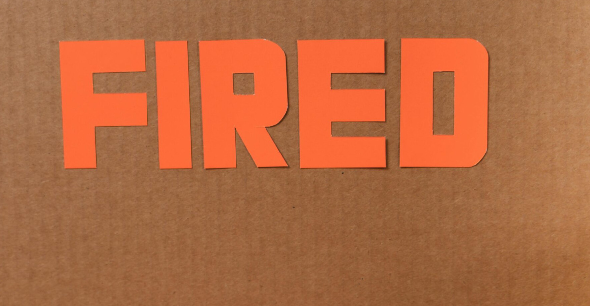 Close-up of a cardboard box labeled FIRED on a wooden table with crumpled papers.