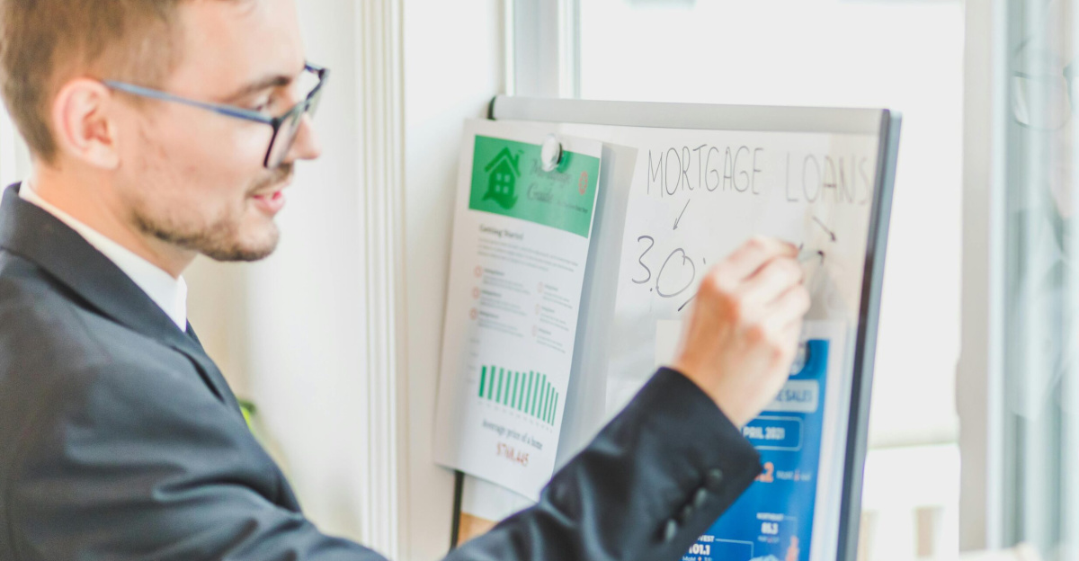 Businessman in suit writes on whiteboard displaying mortgage loan rates during a real estate meeting.