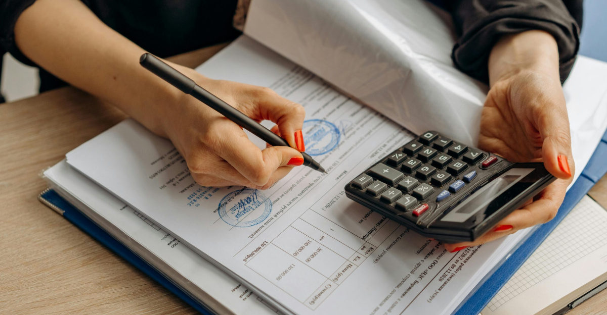 An accountant using a calculator and signing paperwork, showcasing financial analysis.