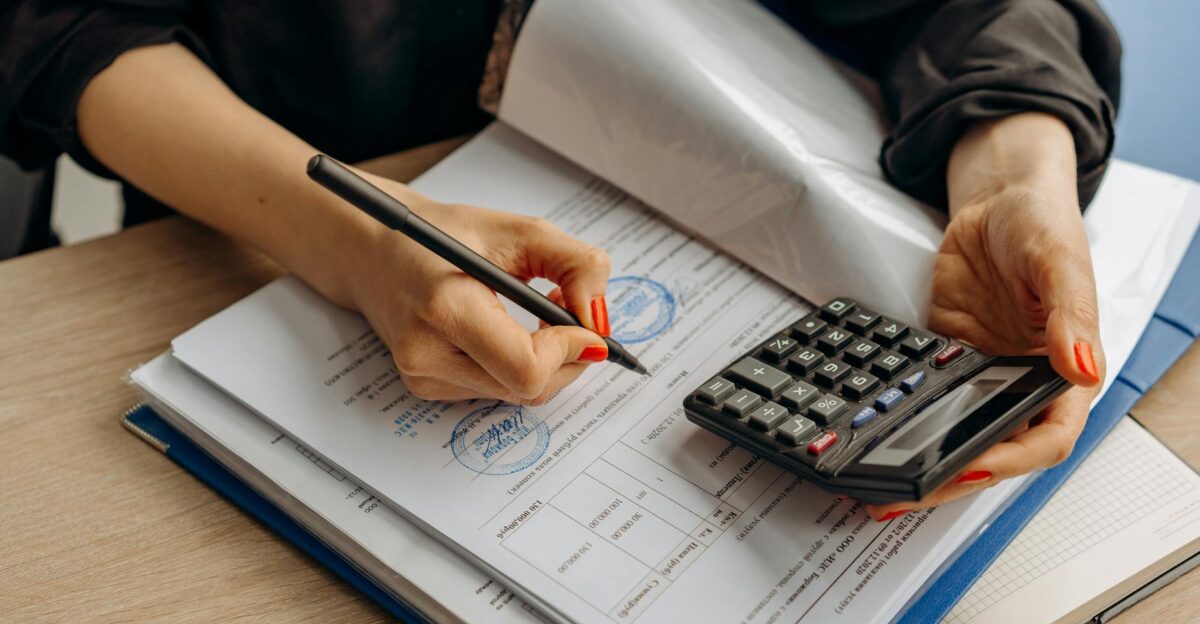 An accountant using a calculator and signing paperwork showcasing financial analysis