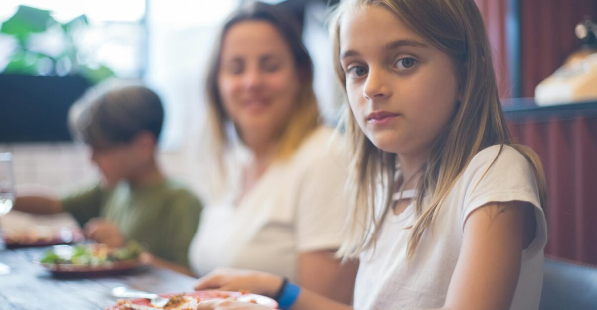 A family enjoying a meal together focusing on a young girl at the dining table
