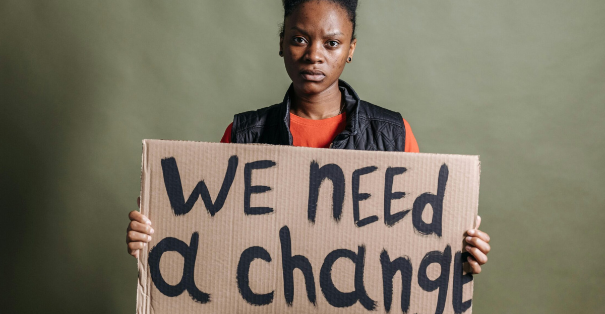 Portrait of an activist with a placard stating 'We need a change', highlighting human rights.