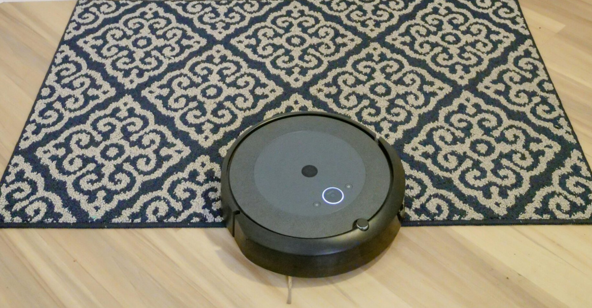 A modern robotic vacuum cleaner operating on a patterned rug near a white door.