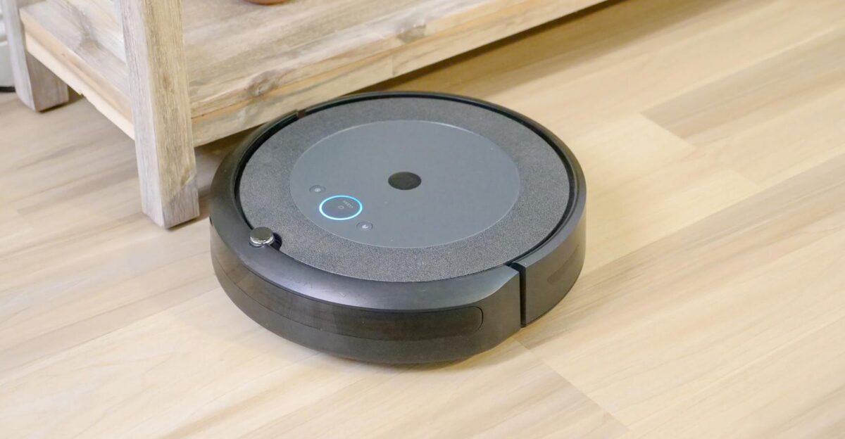 Automated robotic vacuum cleaner on hardwood floor next to plant