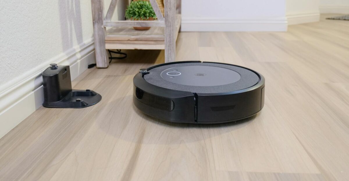 A sleek robotic vacuum navigates a clean hardwood floor beside a docking station