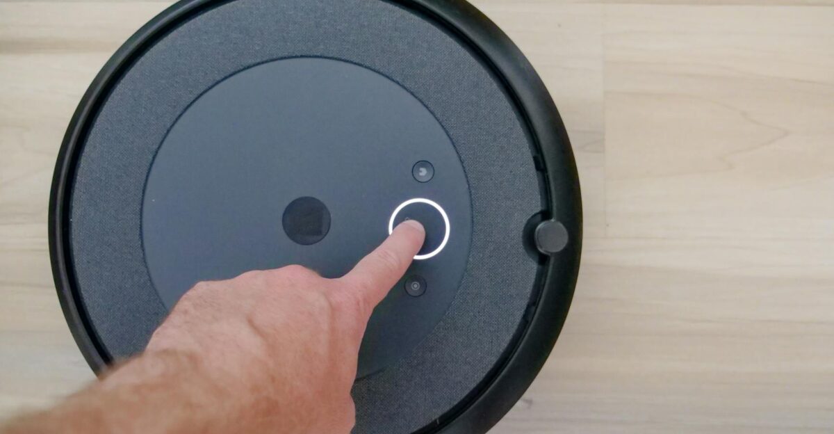 Close-up of a finger pressing a start button on a robotic vacuum cleaner at home
