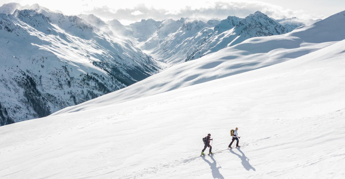Two skiers climbing a sunlit snowy mountain slope in Ischgl, Austria, during winter.