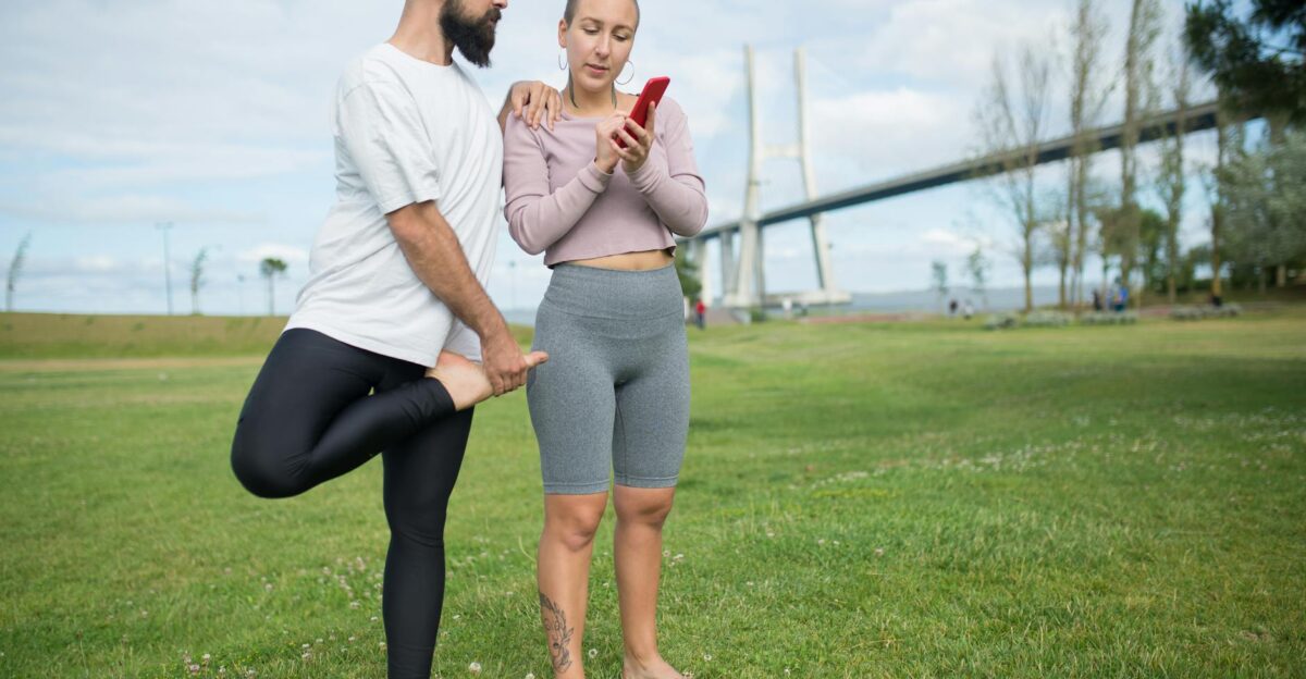 A couple practicing yoga in a park with a stunning bridge in Lisbon as a background using a smartphone for guidance