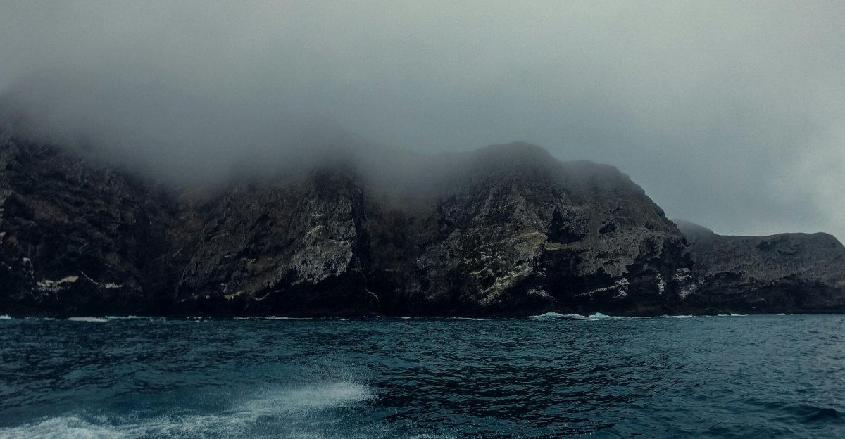 A dramatic seascape featuring fog-covered cliffs and crashing ocean waves under cloudy skies.