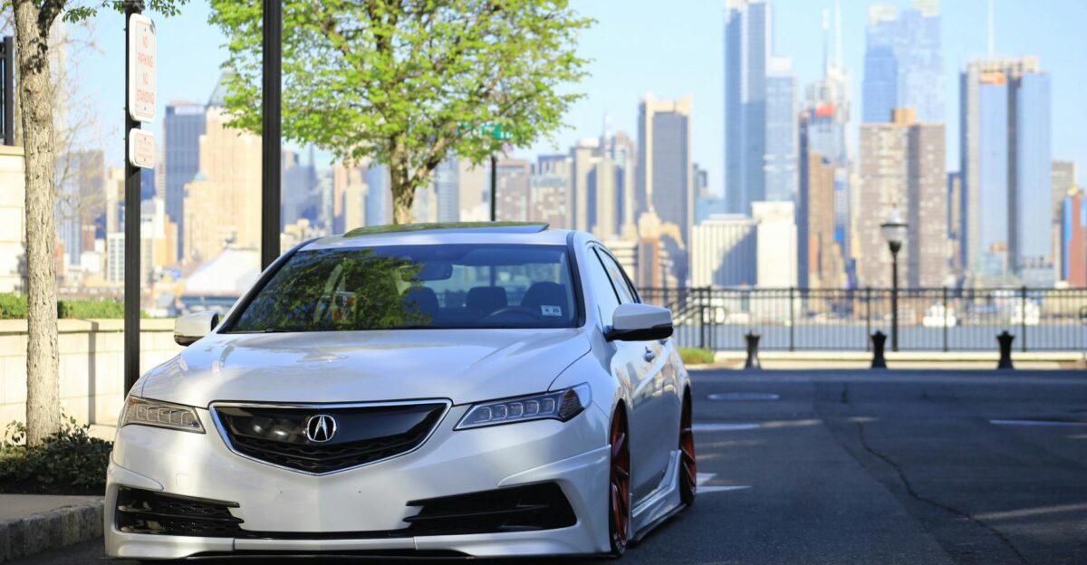 A customized silver Acura parked with a city skyline backdrop showcasing urban car culture