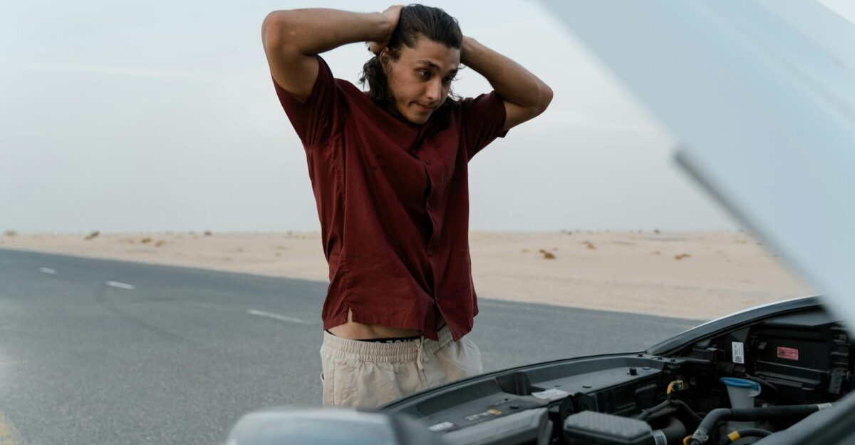 A frustrated man examining a broken car engine on a deserted road showing stress and concern