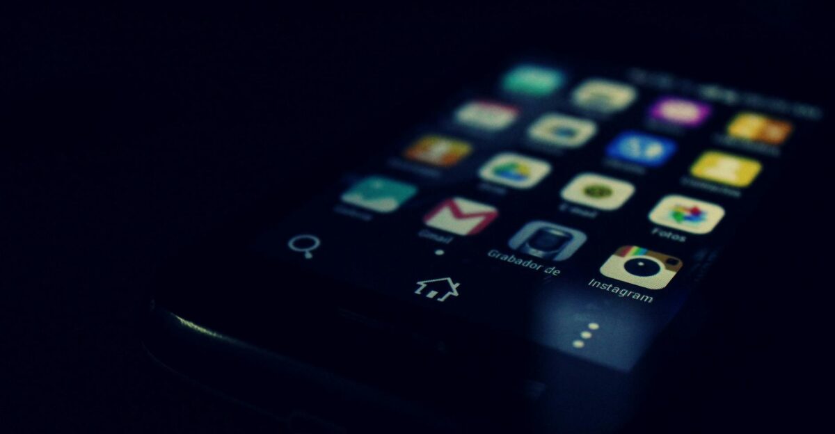 Dark-themed close-up of a smartphone screen highlighting various apps and touchscreen technology