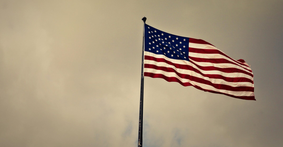 US flag waving in wind against a cloudy sky, symbolizing freedom and patriotism.