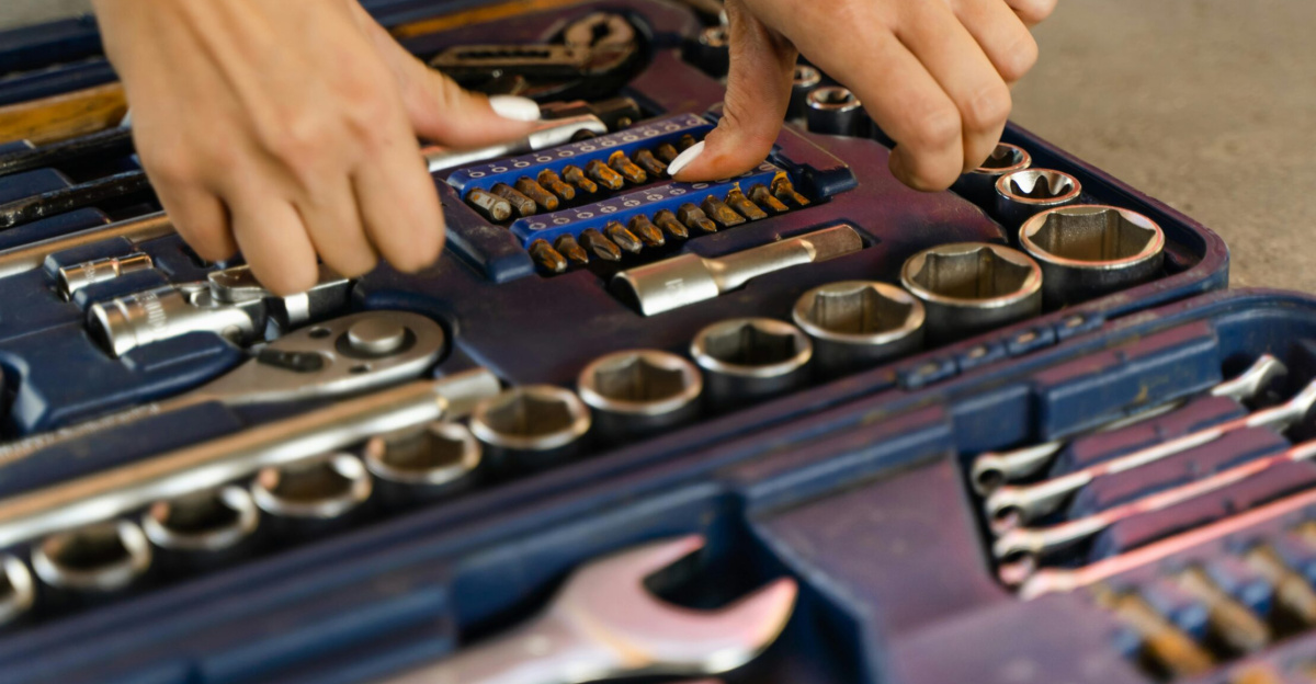 Hands selecting tools from a well-organized toolbox on a concrete surface.