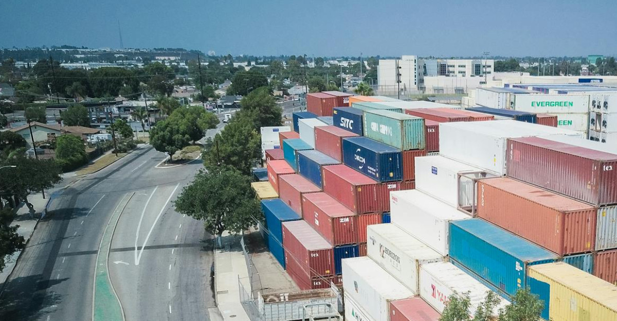 Drone shot showcasing an organized stack of colorful shipping containers by an empty road