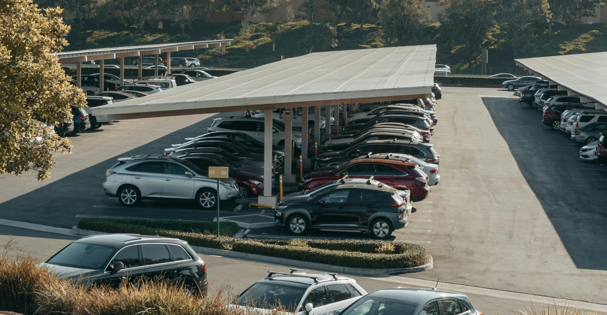 View of a large parking lot with solar panel shades and diverse vehicles parked.