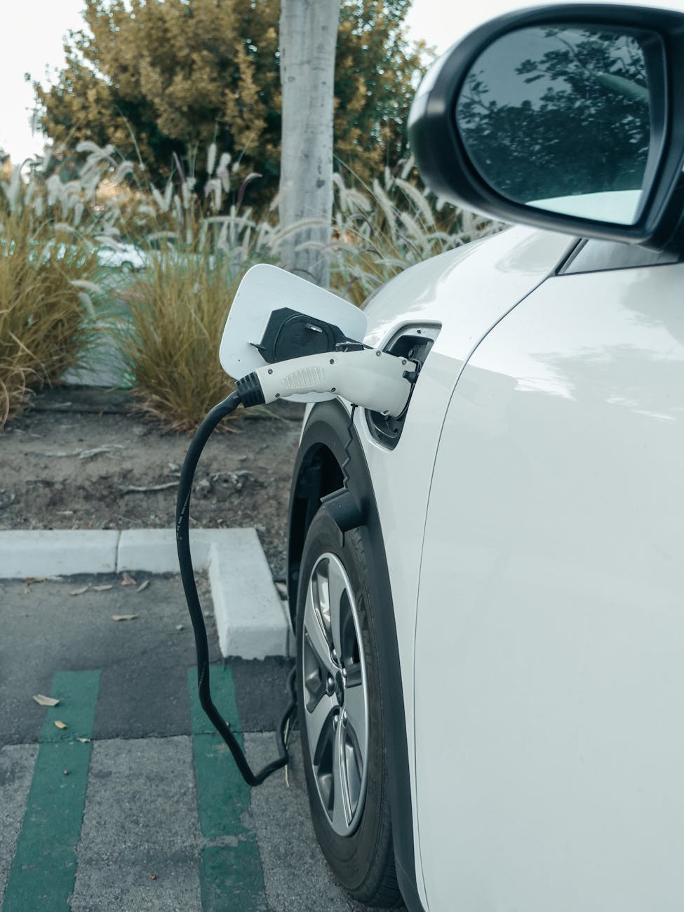 A white electric car plugged into a charger at an outdoor parking area promoting clean energy