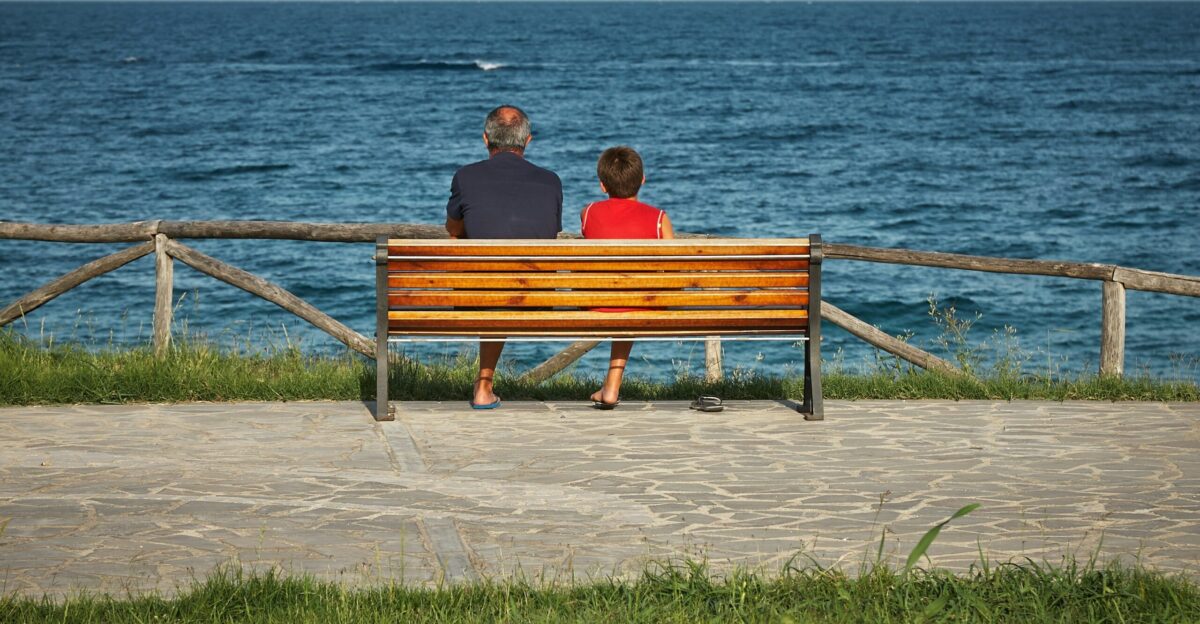 two person sitting on bench beside body of water