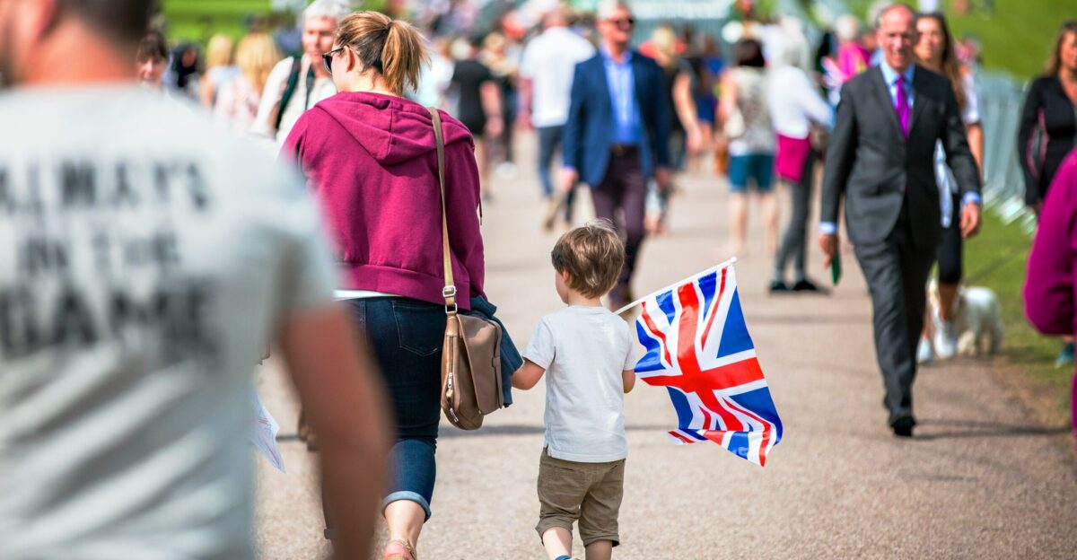 selective focus photography of boy holding U K flag walking on pathway full of people