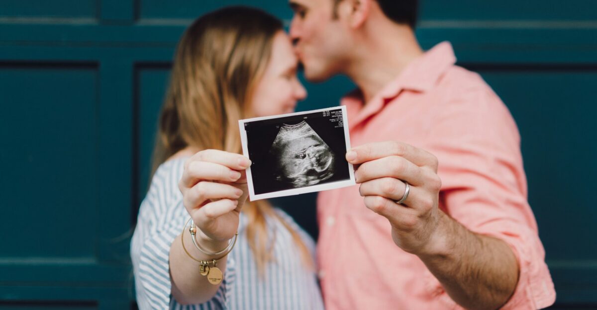 man kissing woman s forehead white holding ultrasound photo