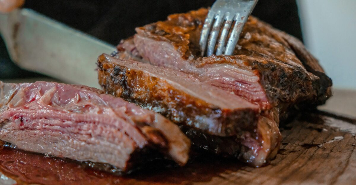 person slicing a meat on brown wooden board