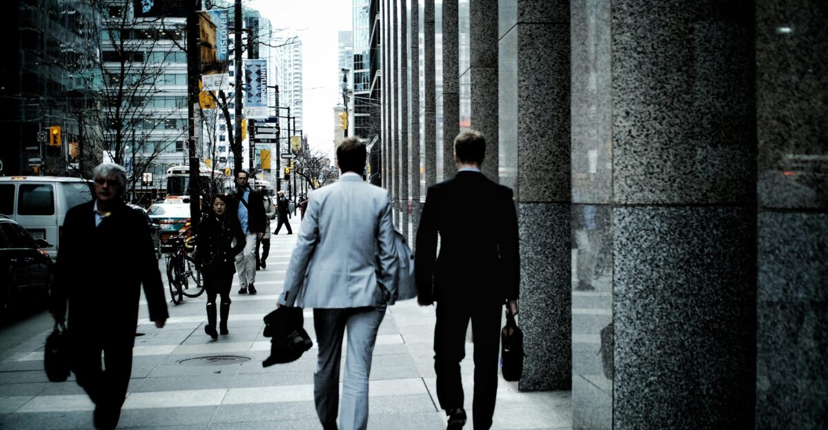 people walking on sidewalk pathway beside road with vehicles and high-rise buildings during daytime