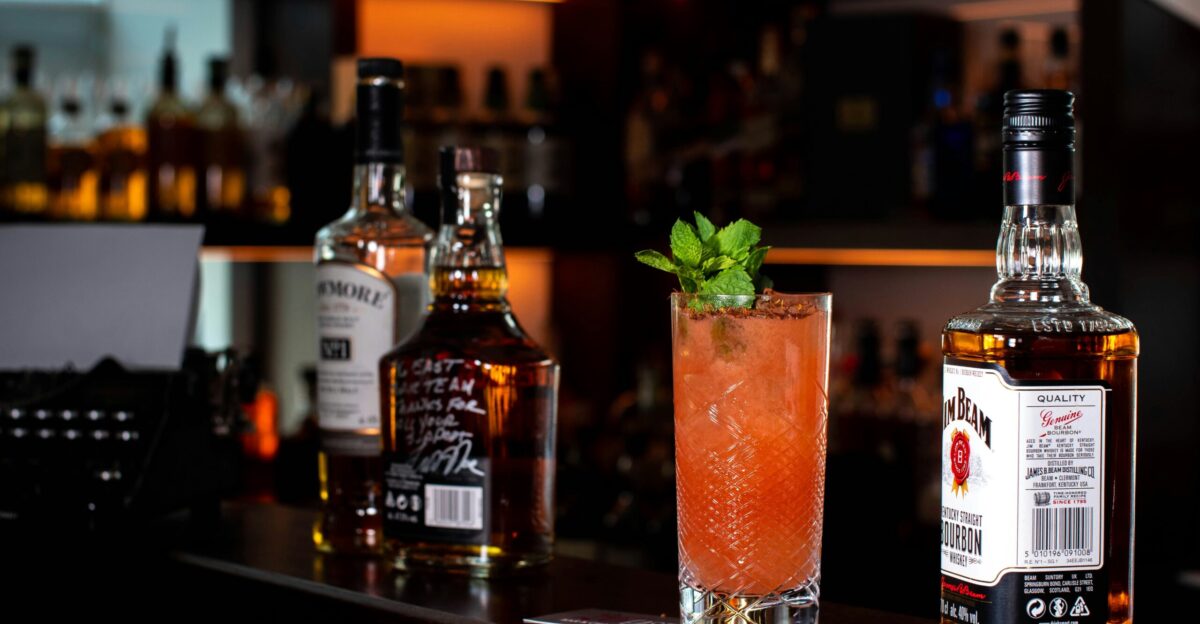 three liquor bottles and cocktail drink on bar counter
