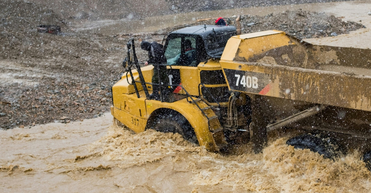 a yellow bulldozer driving through a muddy river