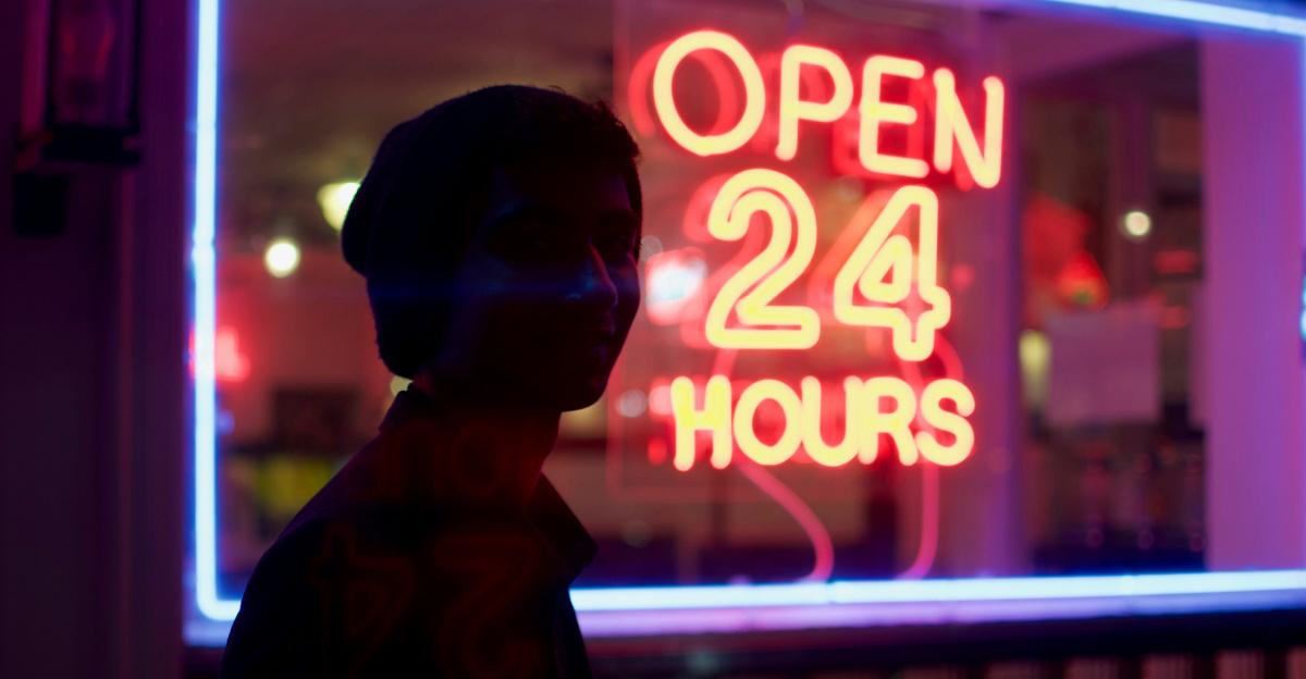 man standing beside open 24 hours signage during nighttime