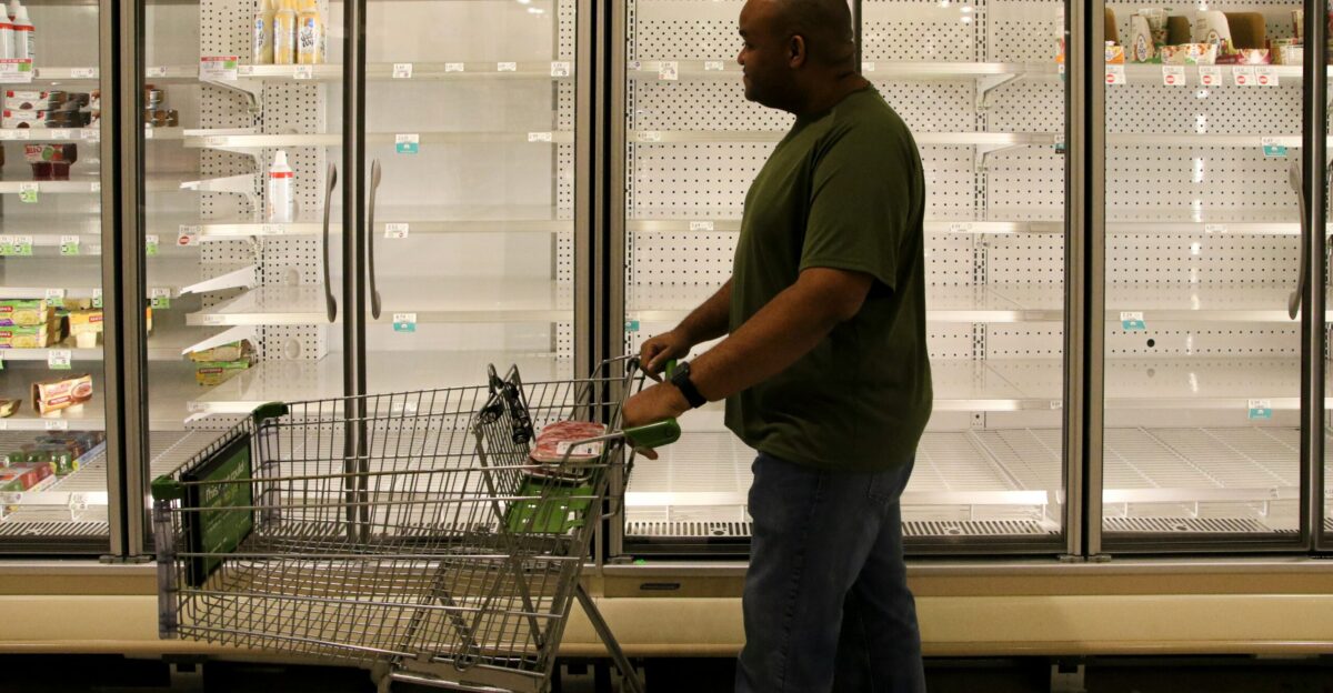 man in brown polo shirt and gray pants standing beside shopping cart
