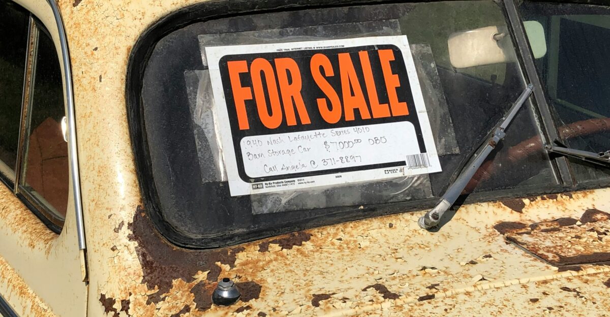 a rusted out car with a for sale sign on it