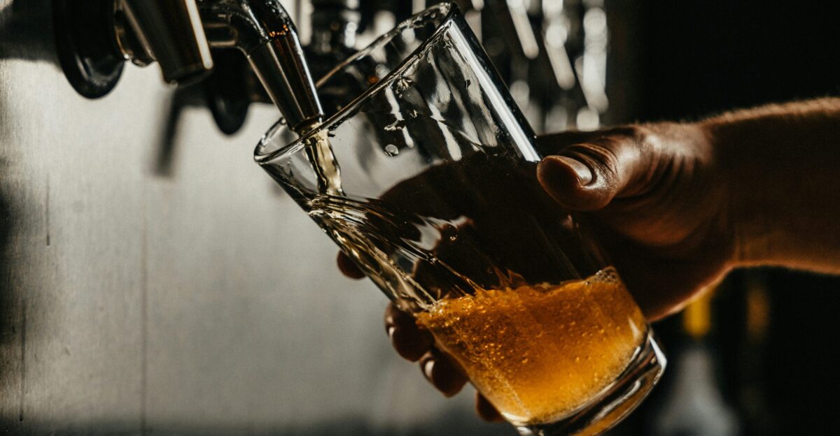 person pouring brown liquid on clear drinking glass