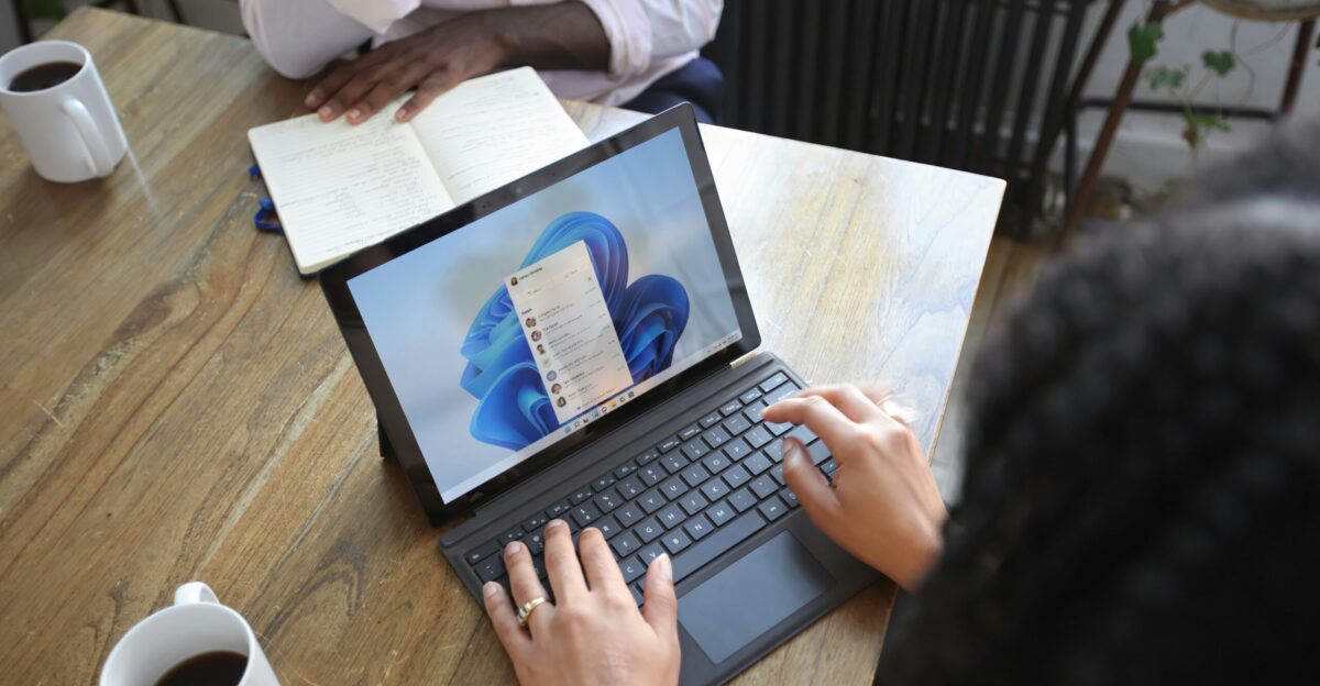 Overhead view of two people at a table working with a Microsoft laptop and notebook